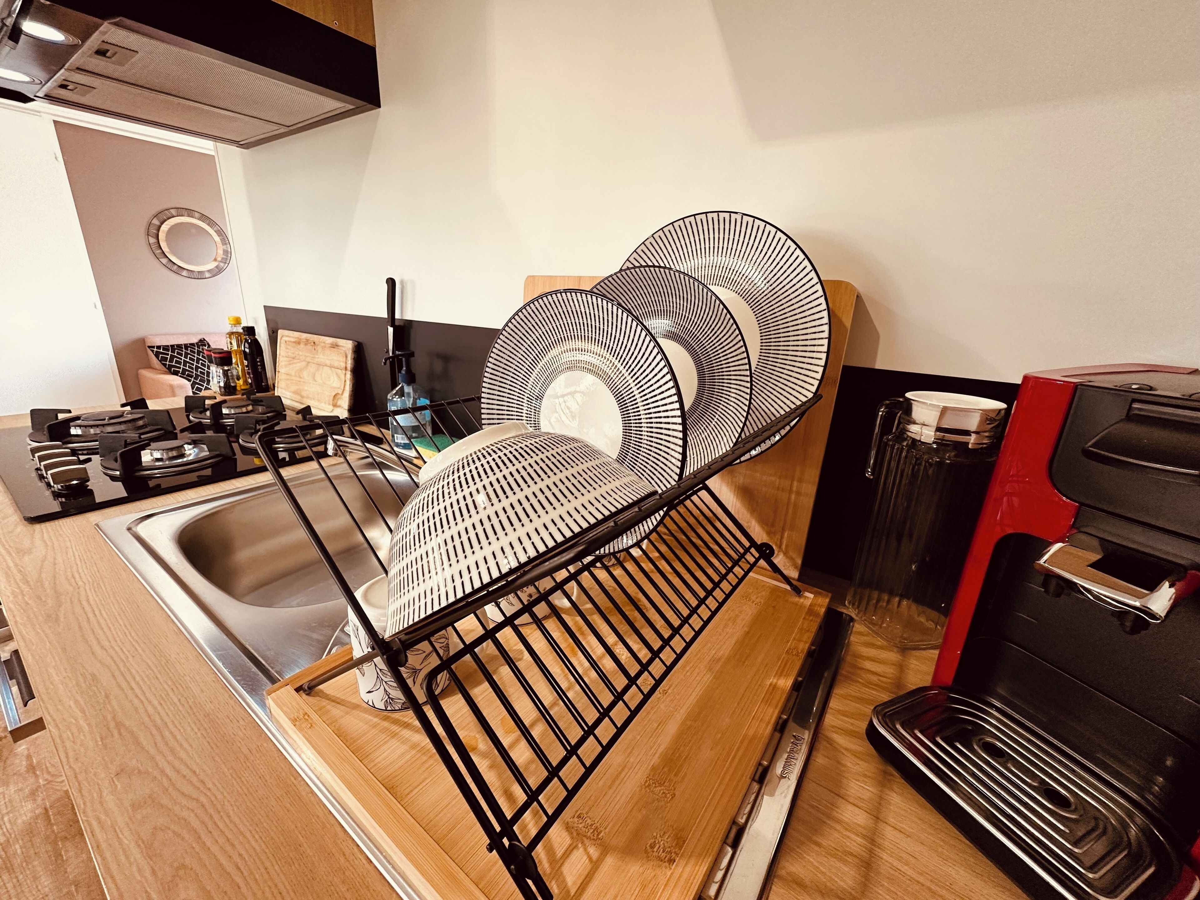 A kitchen with a dish rack, sink, stove, and a coffee machine.