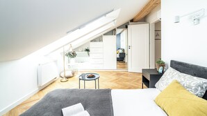 Ein modernes Schlafzimmer mit Dachfenster, einem Bett mit grauem und gelben Kissen, einem kleinen runden Tisch mit einer Schüssel und einem weißen Kleiderschrank.
