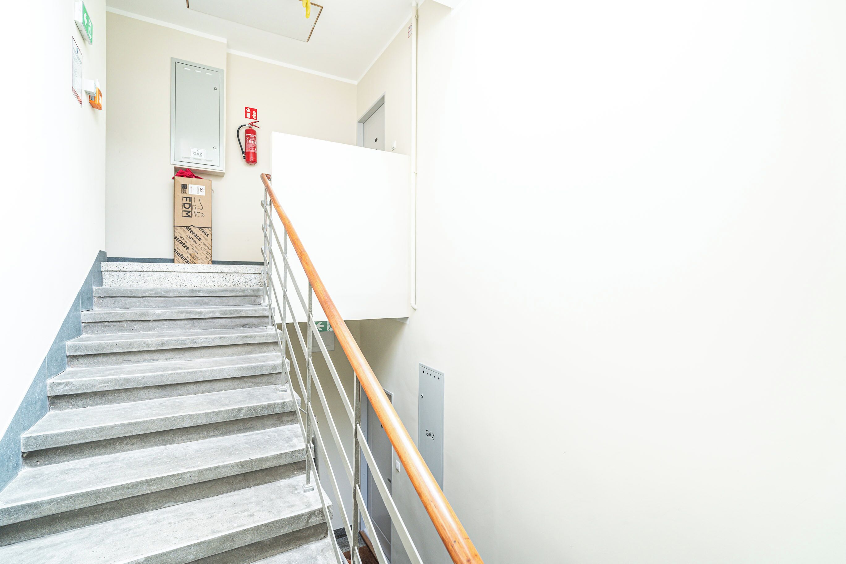 A staircase with a wooden handrail, a fire extinguisher, and a wall-mounted electrical panel.