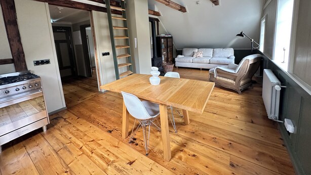 A loft-style living space with a wooden dining table, white chairs, a sofa, and a ladder. - Gamla Apótekið (The Old Pharmacy)  in heart of Akureyri - South Apartment (Akureyri)