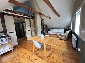 A loft-style living space with a wooden dining table, white chairs, a sofa, and a ladder. - Gamla Apótekið (The Old Pharmacy)  in heart of Akureyri - South Apartment (Akureyri)