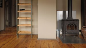 A room with a wooden floor, a metal ladder, a white wall, and a wood-burning stove. - Gamla Apótekið (The Old Pharmacy)  in heart of Akureyri - South Apartment (Akureyri)