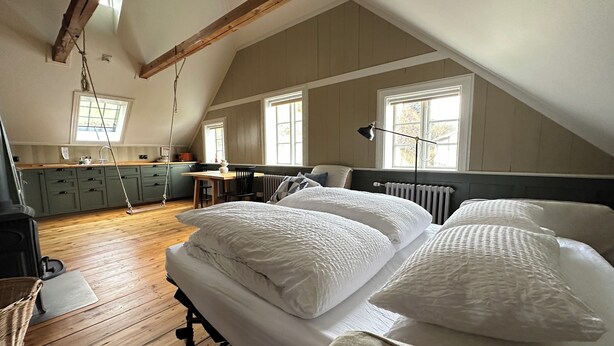 Une chambre confortable située dans les combles, avec un grand lit, un plancher en bois et une cuisine à l’arrière-plan.