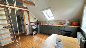 Une cuisine avec un plancher en bois, une cuisinière, un évier et une fenêtre.