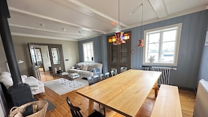 A spacious living room with a wooden dining table, black chairs, and a sofa. There is a large window providing natural light and a view of the outside. - Gamla Apótekið (The Old Pharmacy)  in heart of Akureyri - Main apartment (Akureyri)