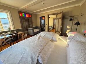 A bedroom with a bed, a desk, a chair, a radiator, a window, and a door.