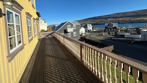 A wooden deck with a railing overlooking a street with buildings and a lake. - Gamla Apótekið (The Old Pharmacy)  in heart of Akureyri - Main apartment (Akureyri)