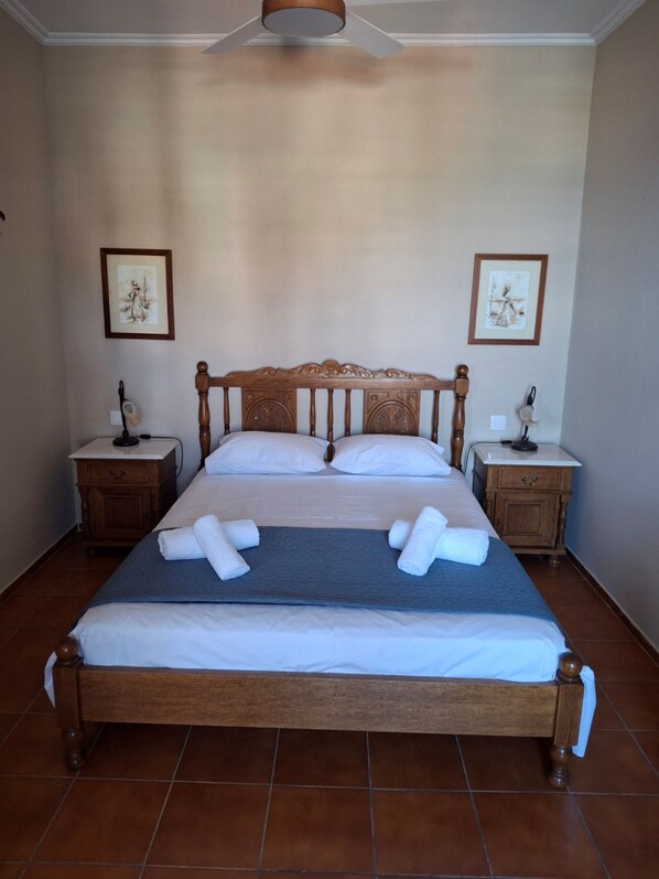 A neatly made bed with white linens and two pillows, flanked by wooden nightstands with framed pictures and small lamps. - Villa Hydra Estrella (Hydra)