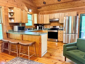 A wooden cabin interior with a kitchen featuring a stainless steel refrigerator, oven, and microwave, wooden cabinets, and a bar stool area.