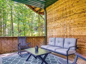 Un'area salotto esterna coperta con un muro in legno, una panca, un tavolo e vista su una foresta.