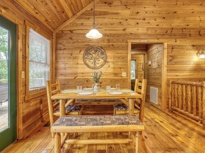 Un interior de madera con una mesa de comedor dispuesta para cuatro personas, rodeada de sillas con cojines estampados.