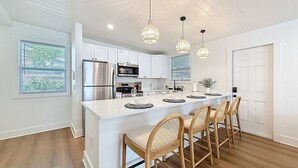 A modern kitchen with white cabinetry, stainless steel appliances, and a central island with bar stools.