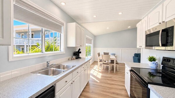 A modern kitchen with white cabinetry, a stainless steel sink, and a black stove.