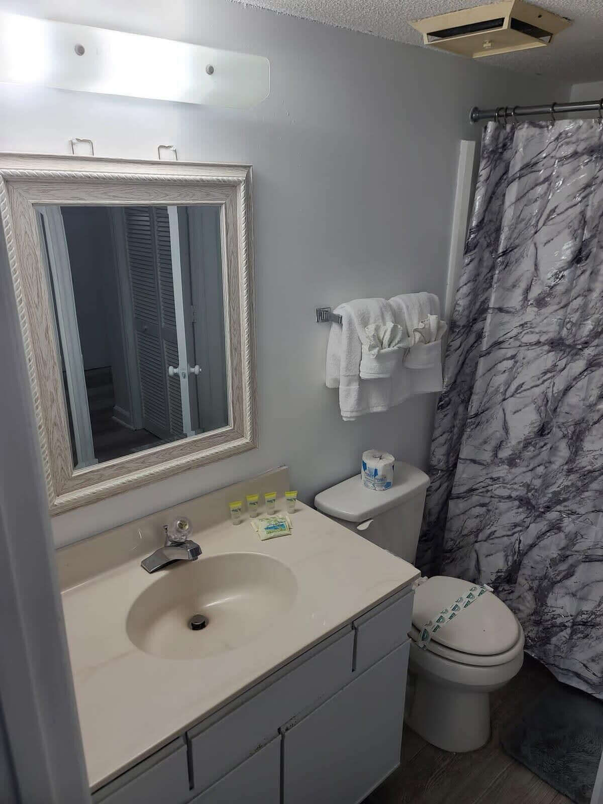A bathroom with a white sink, a mirror with a wooden frame, a toilet, and a shower curtain with a marble pattern.