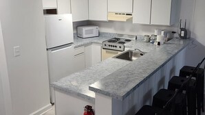 Una cocina moderna con armarios blancos, encimera de granito, estufa, microondas y pileta. Hay taburetes negros a lo largo de la encimera.
