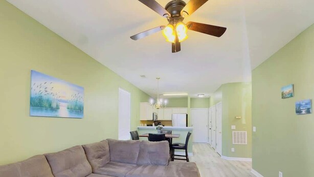A living room with a sectional sofa, a ceiling fan, and a dining area in the background.