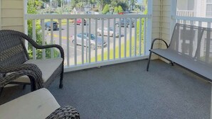 A covered balcony with wicker furniture and a view of a parking lot and trees.
