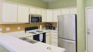 A kitchen with white cabinets, a stainless steel refrigerator, a microwave, a stove, and a coffee maker.
