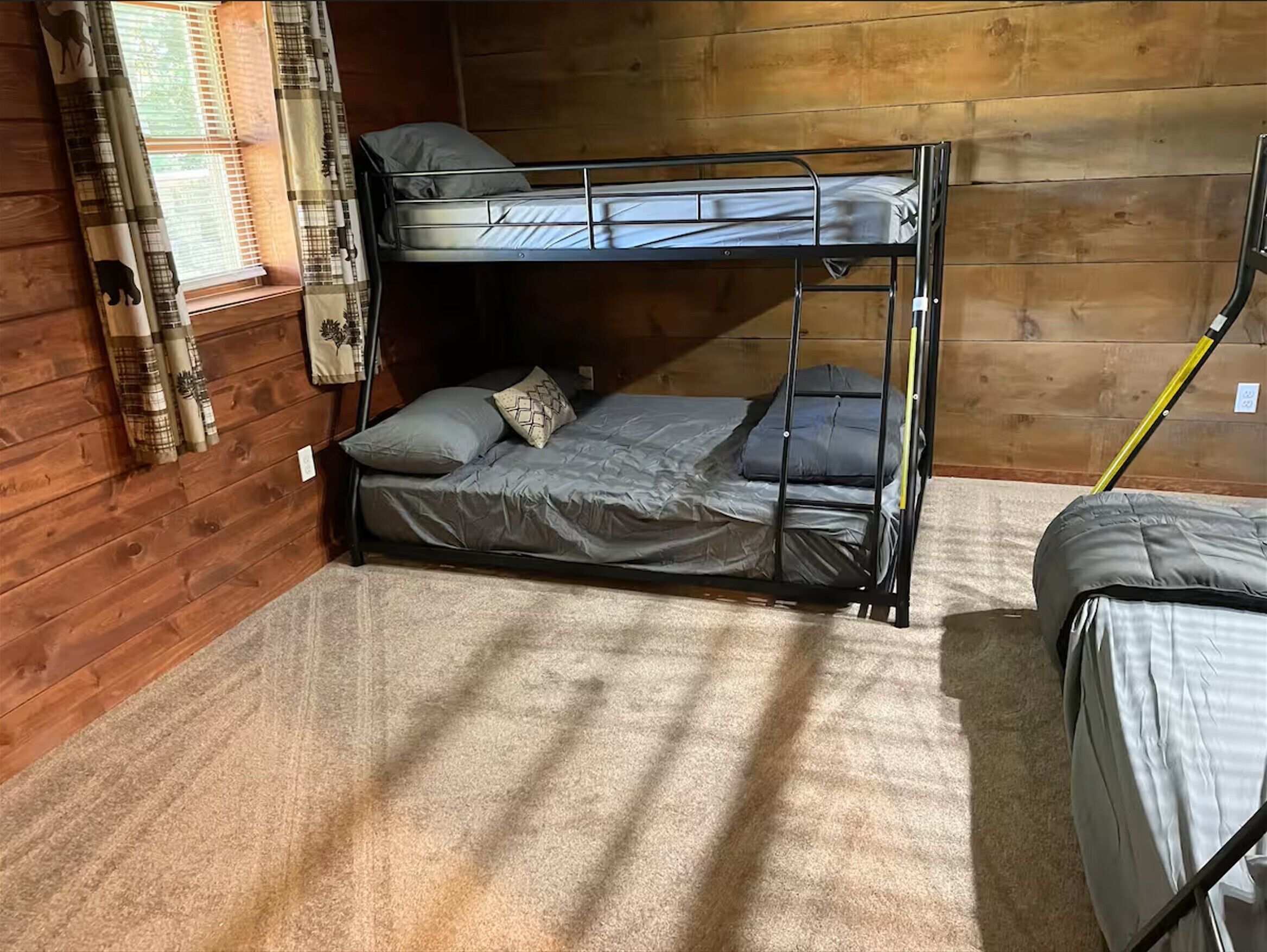 A bunk bed in a wooden cabin room with a window, curtains, and a small table.