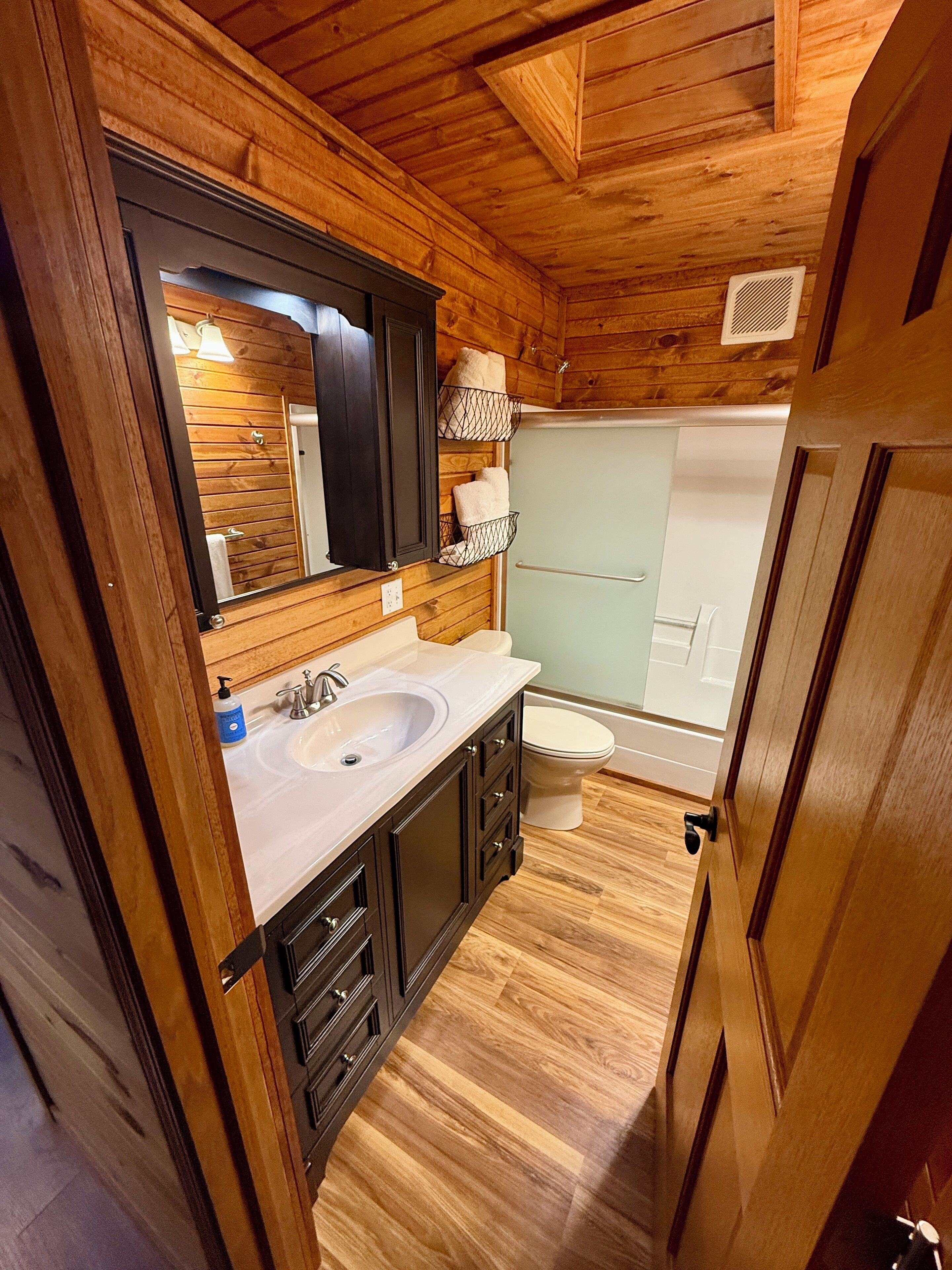 Une petite salle de bain en bois, équipée d’un lavabo, d’un miroir et d’une cabine de douche.