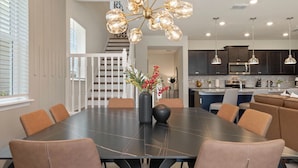 Een moderne eetruimte met een grote donkere tafel, beklede bruine stoelen en een decoratieve lamp.