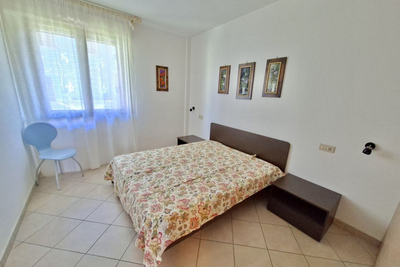 A bedroom with a bed, a chair, a nightstand, and three framed pictures on the wall.