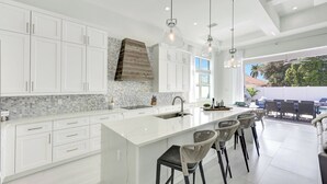 Une cuisine moderne avec des meubles blancs, un grand îlot central doté de tabourets et un éclairage suspendu.