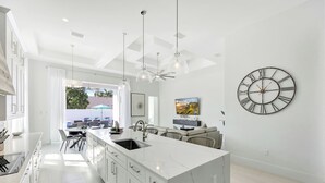 Une cuisine moderne dotée d’un grand îlot central, de meubles blancs et d’un éclairage suspendu.