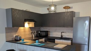 A modern kitchen with dark cabinetry, a stainless steel refrigerator, a microwave, and a wooden island with bar stools. - Orient blue garden, direct access 50m from the beach! (Baie orientale)