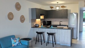 A modern kitchen with a central island, black bar stools, and a ceiling fan. - Orient blue garden, direct access 50m from the beach! (Baie orientale)