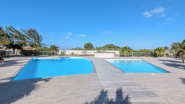 A swimming pool area with two pools, surrounded by a wooden deck and a paved walkway. - Orient blue garden, direct access 50m from the beach! (Baie orientale)