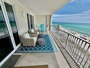 En balkon med fletningsmøbler, et mønstret tæppe og udsigt til stranden.