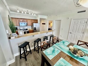 Une cuisine moderne avec des meubles en bois, un réfrigérateur en acier inoxydable et un coin repas comprenant une table et des tabourets de bar.