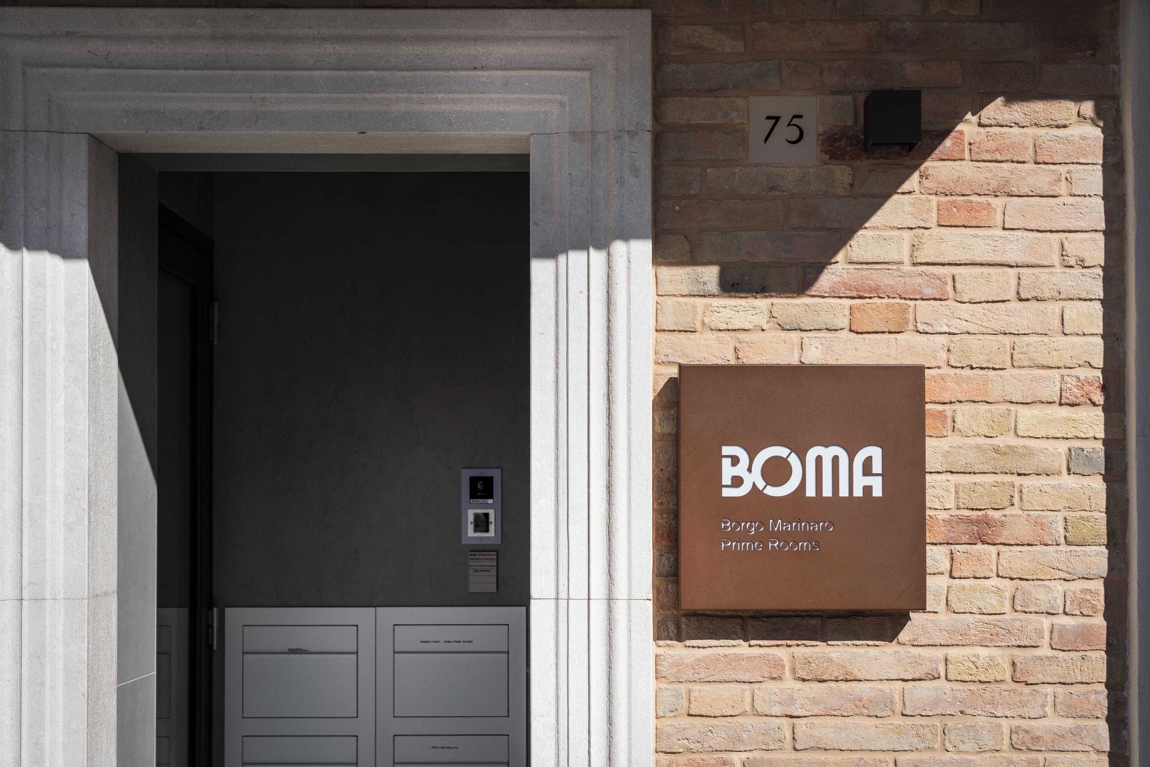 Een gebouw ingang met een bord waarop staat 'BOMA Borg's Marinetto Prime Rooms' en het cijfer '75' op een bakstenen muur.