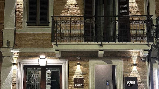 Un edificio de dos pisos con un balcón y una entrada a nivel de calle, con un letrero que dice 'BUCCIA'.