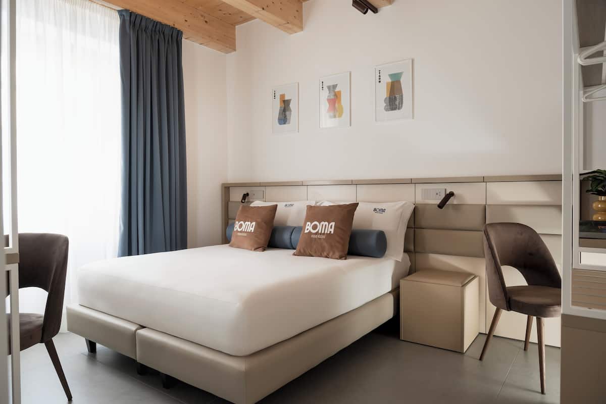 Een moderne hotelkamer met een groot bed, twee kussens, een nachtkastje, een stoel en kunst aan de muur.