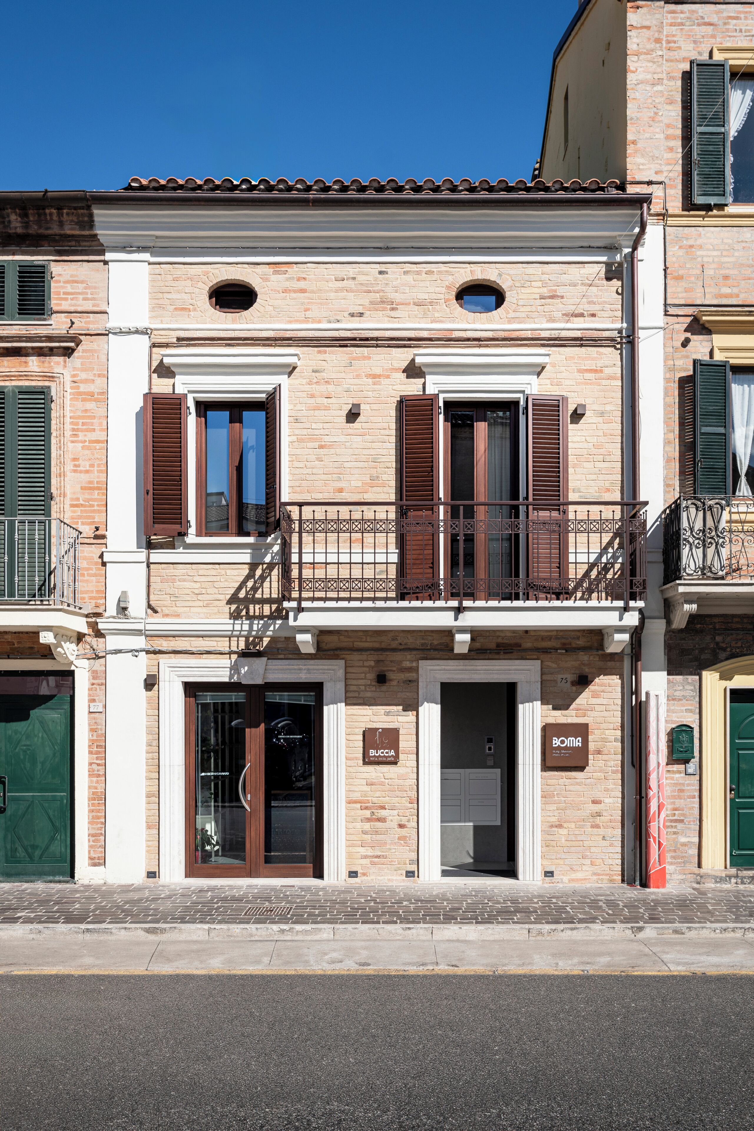 Un edificio de dos pisos con un balcón, una entrada a una tienda y una puerta verde.