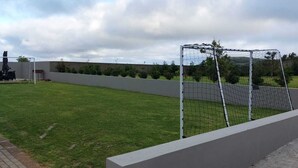 Un espacio al aire libre cercado con un campo de césped, un arco de fútbol y un camino pavimentado.