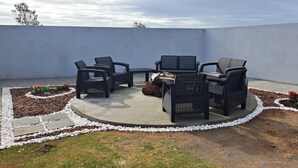 Un espacio de estar al aire libre circular con una chimenea, rodeado por un jardín de guijarros blancos y plantas.