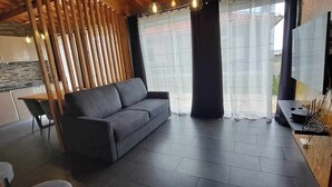 Una sala de estar moderna con un sofá gris, una mesa de comedor y una cocina al fondo.
