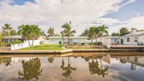A residential area with houses, palm trees, and a calm water body reflecting the surroundings.