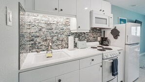 A modern kitchen with white cabinets, a tiled backsplash, a microwave, a stove, and a refrigerator.