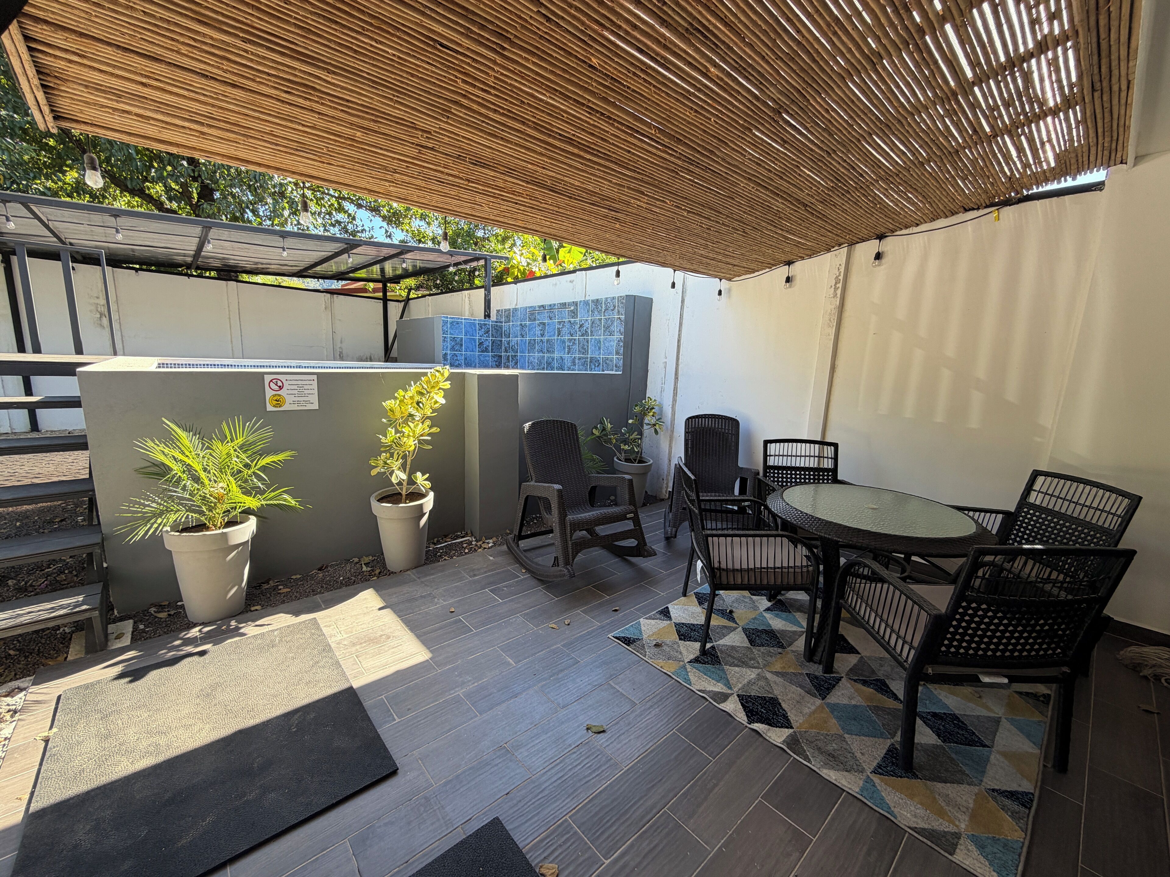 An outdoor patio area with a bamboo ceiling, potted plants, and a round table with chairs.