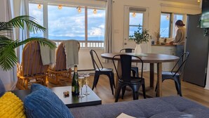 Un salon moderne comprenant un canapé, une table à manger avec des chaises, un coin cuisine et de grandes fenêtres offrant une vue dégagée.