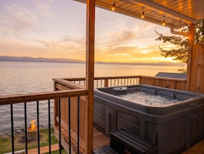 Un bain à remous sur une terrasse en bois, avec vue sur un lac et des montagnes au coucher du soleil.