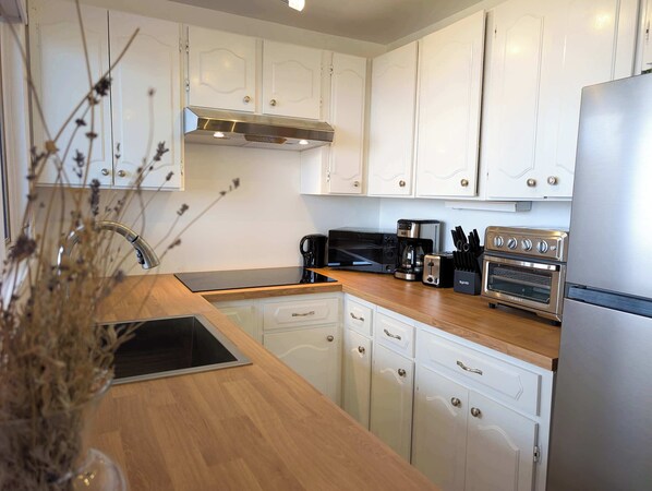 A modern kitchen with white cabinets, a stainless steel range hood, a black microwave, a coffee maker, a toaster, and a double oven.