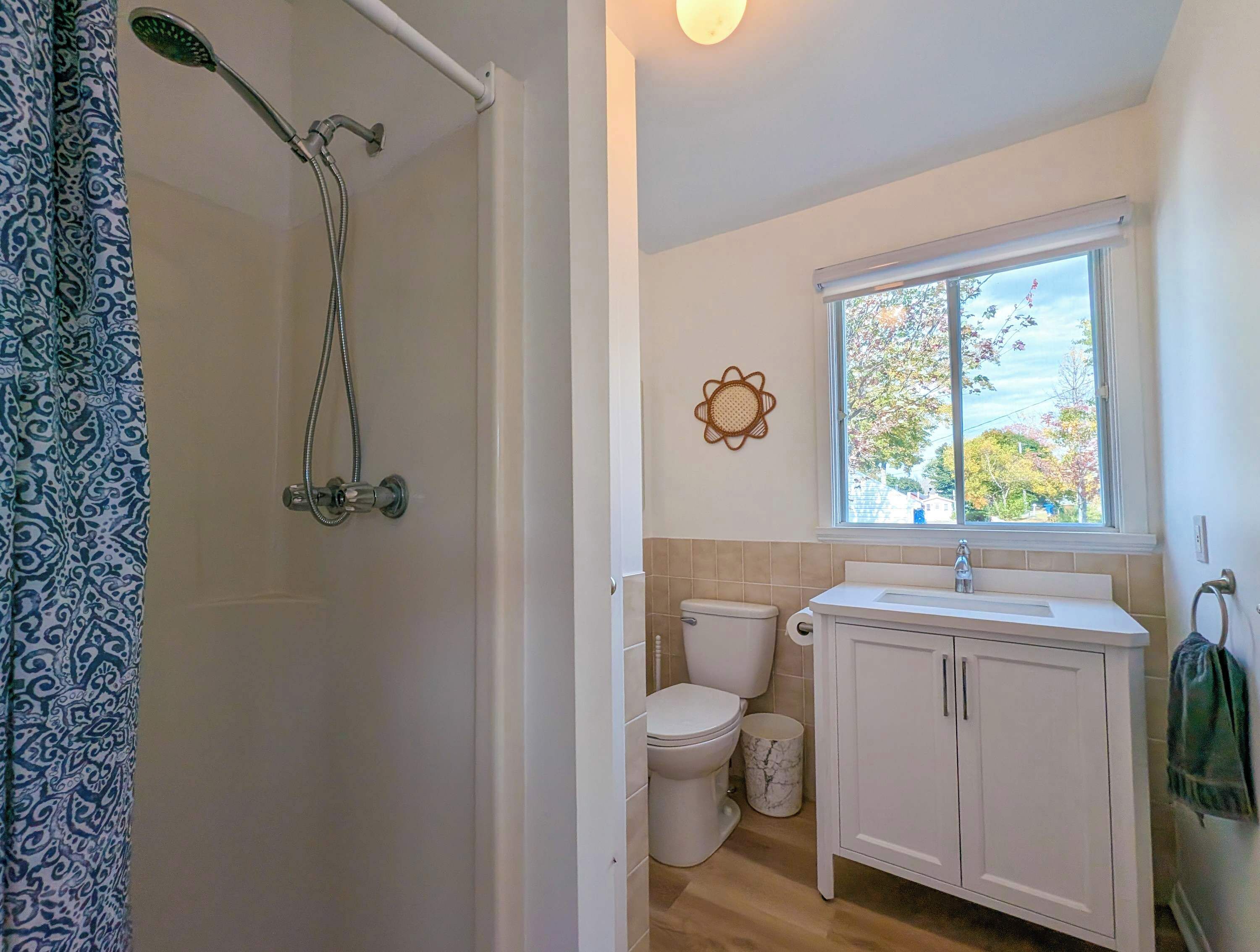 A bathroom with a shower, toilet, sink, and window.