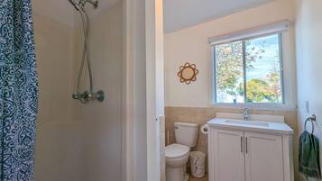 A bathroom with a shower, toilet, sink, and window.