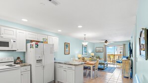 A modern kitchen with white cabinets, a microwave, a refrigerator, and a dining area with a table and chairs. - Spacious condo, across the street from the beach + Free Attraction Tickets! (North Myrtle Beach)