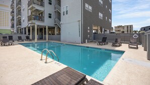 A swimming pool with lounge chairs and a building with balconies. - Spacious condo, across the street from the beach + Free Attraction Tickets! (North Myrtle Beach)